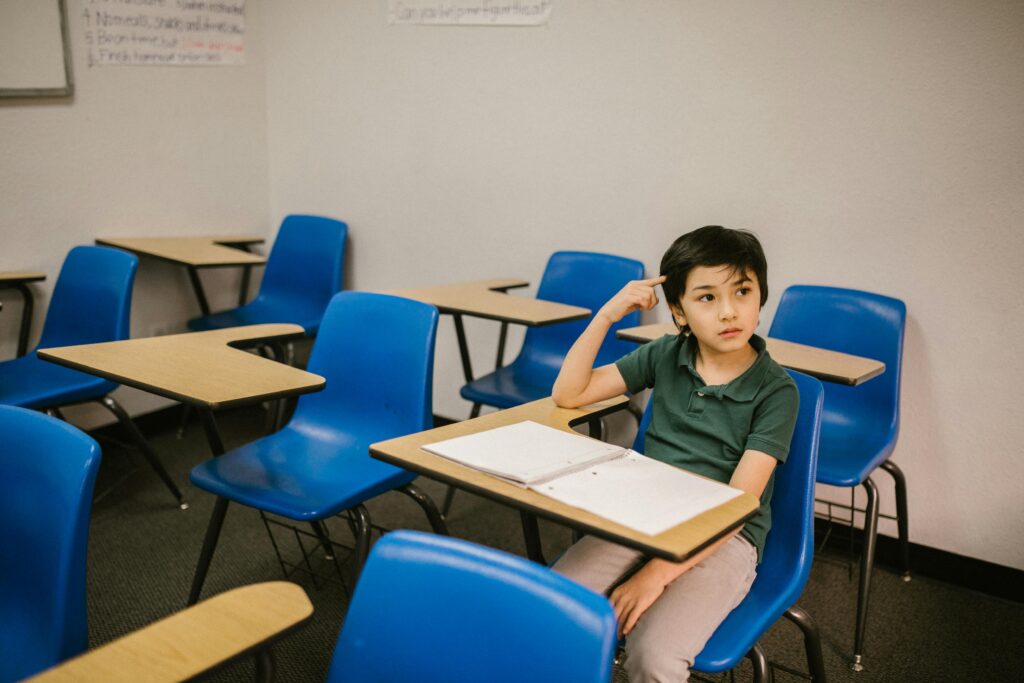 A young boy appears thoughtful while sitting alone in a classroom.