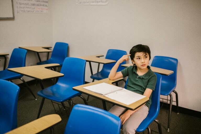 A young boy appears thoughtful while sitting alone in a classroom.