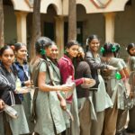 Group of smiling schoolgirls with braids standing outdoors during lunchtime at school.